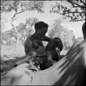 Man sitting in the shade with a child lying across his lap, another man sitting near them