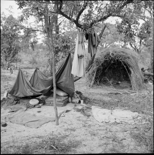 Expedition equipment partially covered by a tarpaulin, with blankets hanging from a line next to it, skerm with blankets on the floor of it in the background