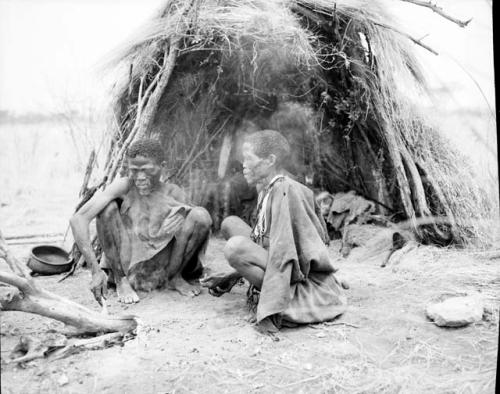 "Old /Gaishay" sitting with his wife, Di//khao!na, by their fire in front of their skerm