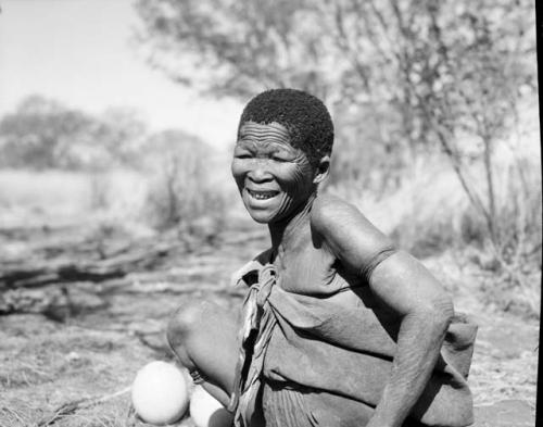 Woman sitting, with two ostrich egg shells on the ground next to her