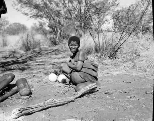 Woman sitting, with two ostrich egg shells on the ground next to her