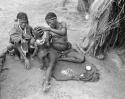 Khwo//o-/Gasa looking at a child, with ostrichegg shell beads on a kaross on the ground in front of her, sitting with "Old /Gam"