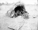 Ti//khao (headman of Band 7, brother of Xama) and his wife, /Khoa, sitting in front of a skerm with a group of people