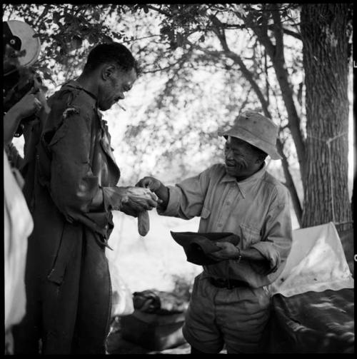 ≠Toma wearing Western clothing, handing tobacco to Venter