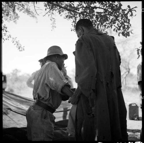 ≠Toma wearing Western clothing, handing tobacco to Venter, view from behind