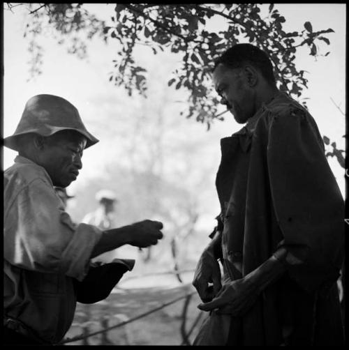 ≠Toma wearing Western clothing, handing tobacco to Venter