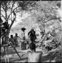 Tsamgao wearing Western clothing, sitting on a jerry can, facing a group of people sitting, including John Marshall, with Venter backing away and mimicking someone