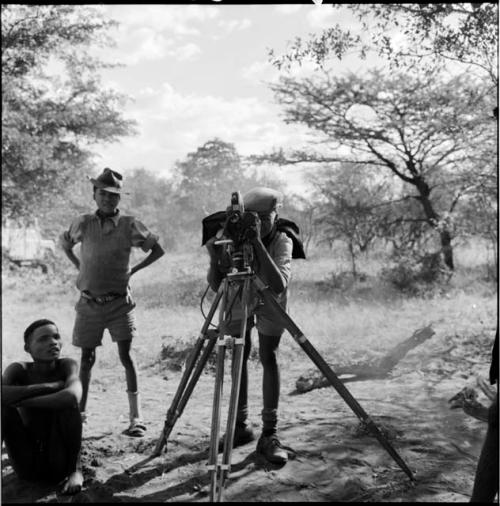 /Gaishay wearing Western clothing, focusing the film camera, with Tsamgao standing next to him, another person sitting near them