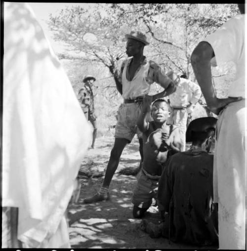 ≠Toma kneeling, signaling to the camera man, with expedition members standing next to him