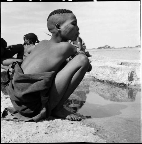 Woman wearing a blanket around her waist, squatting at the edge of a pan