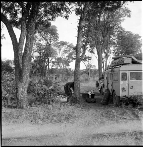 Two expedition members working near the Land Rover, with food on a table next to it