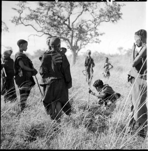 Women and children on a gathering trip, with a woman squatting, digging with her digging stick