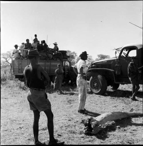 People sitting and standing in the back of an expedition truck, with people standing and another truck parked next to it