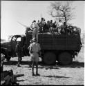 People sitting in the back of an expedition truck, with other people standing next to it