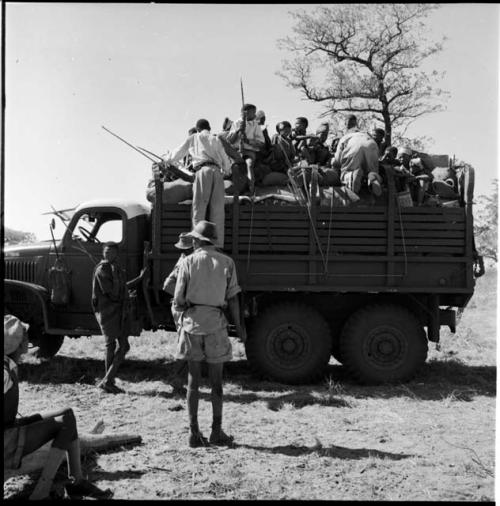 People sitting in the back of an expedition truck, with other people standing next to it