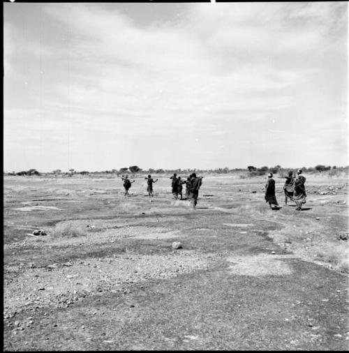 Group of women walking toward a pan, carrying their digging sticks across their shoulders