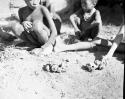 Group of children sitting in front of a skerm, with toy cars made of veldkos on the ground next to them, close-up