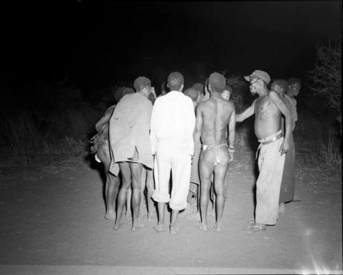 Group of people beginning to dance again at a night dance after an intermission, with /Ti!kay giving them instructions