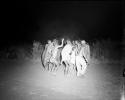 Group of boys dancing in a night dance, with a group of men dancing in a circle around them, distant view