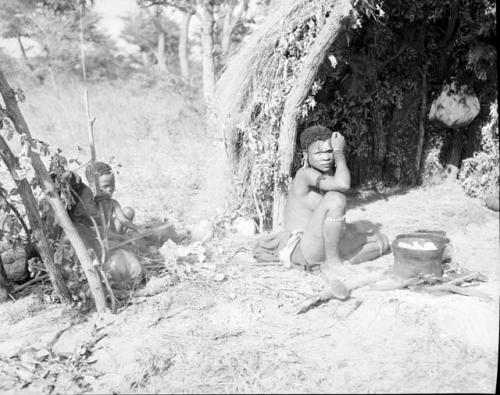 Woman cooking with an iron pot, sitting in front of a skerm, with two children sitting near her