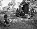 Group of people sitting next to a smoking fire in front of a skerm