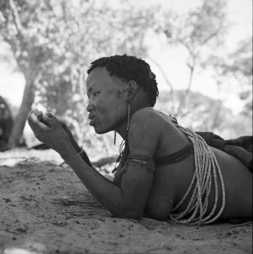 Woman wearing many beads, lying down, propping herself up on her elbows, view from the side