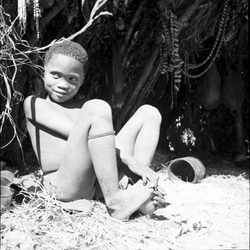 Boy sitting next to a skerm, with tin cans on the ground next to him