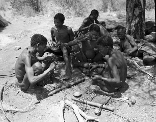 "/Qui Navel" and ≠Gao working on arrows at the werft of ≠Gao (headman of Band 3, son of /Gasa and brother of Gau), sitting with /Goishay (≠Gao's wife), "/Gao Music" (brother of /Goishay) playing the //guashi, ≠Toma (≠Gao and /Goishay's son), Dam (husband of ≠Gisa), Khwo//o (mother of "/Gao Music" and /Goisha), /Naoka (wife of "/Gao Medicine") and !Naishi (brother of /Goishay and "/Gao Music")