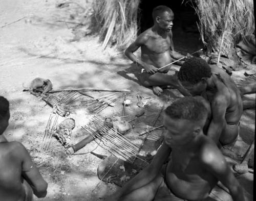 "Gao Helmet" and two other men working on arrows, applying poison from a little bone dish