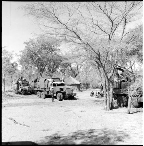 Group of people sitting near three parked expedition trucks, with expedition members on and next to the trucks, skerm in the background