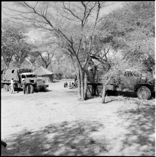 Group of people sitting near two parked expedition trucks, with expedition members on and next to the trucks, skerm in the background