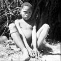 Boy sitting next to a skerm, with tin cans on the ground next to him