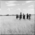 Group of women walking in a line, carrying their digging sticks across their shoulders