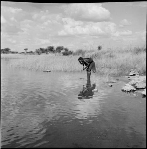 Woman standing in the water in a pan, leaning over, washing her face