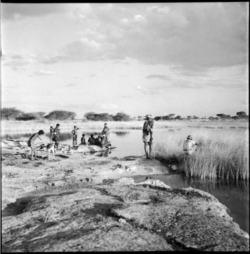 Group of people, including a man wearing Western clothing, standing with a dog at the edge of a pan