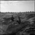 Two men squatting at the edge of a pan