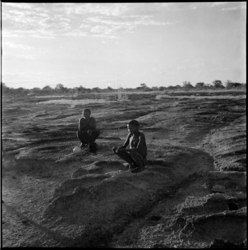 Two men squatting at the edge of a pan