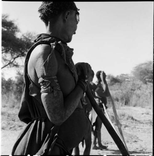 Three women standing, holding poles used for beating mohengo