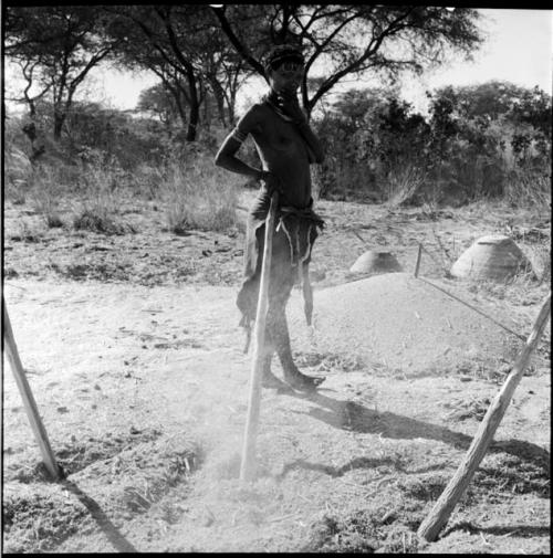 Woman standing next to her pole in the mohengo, with two prepared piles in the background