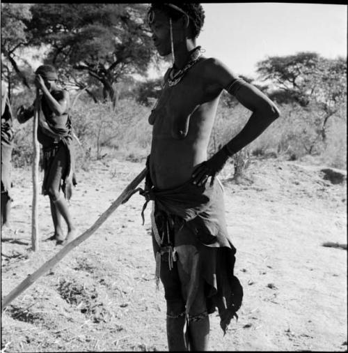 Two women standing, holding poles used to beat mohengo