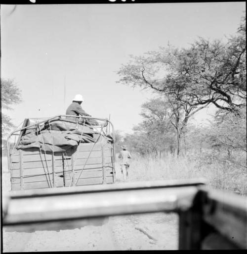 Man wearing a helmet, sitting in the back of an expedition truck, view from behind