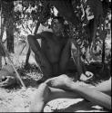 Man sitting in the shade, with another person's feet next to him