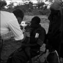 Baby being fed medicine by Robert Story, sitting on Kernel Ledimo's lap