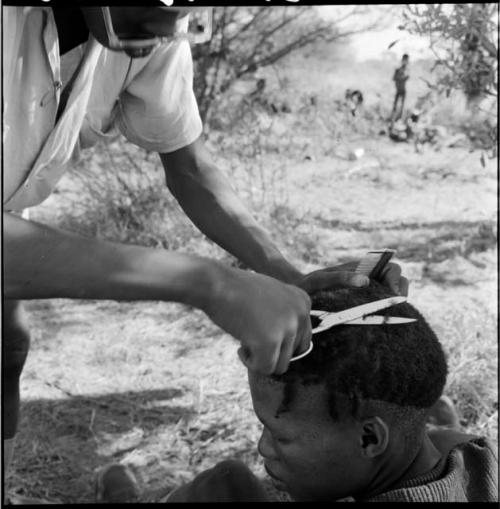 Man wearing Western clothing, standing, cutting another man's hair, close-up