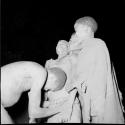 Medicine man curing a woman who standing with two other women, leaning against one of them