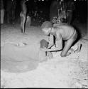 Medicine man curing a sick person lying on the ground, with people in the dance circle in the background