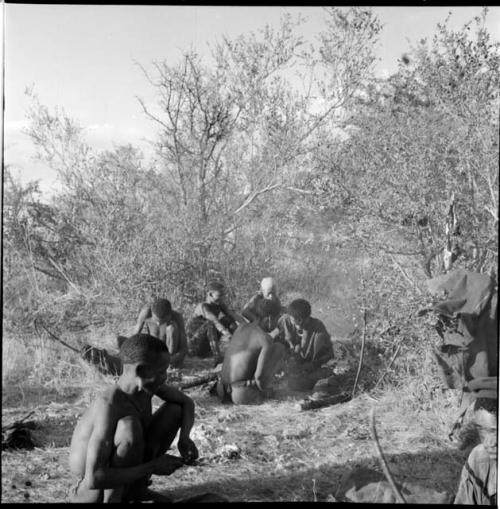 Men squatting, preparing their hunting equipment, with bows, arrows and other hunting equipment on the ground near them