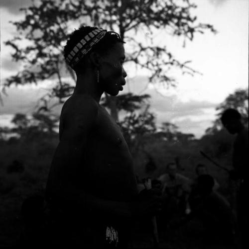 Woman standing, profile, with a tree in the background