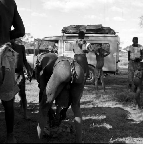 Group of men and boys stand near an expedition truck, with one man leaning over