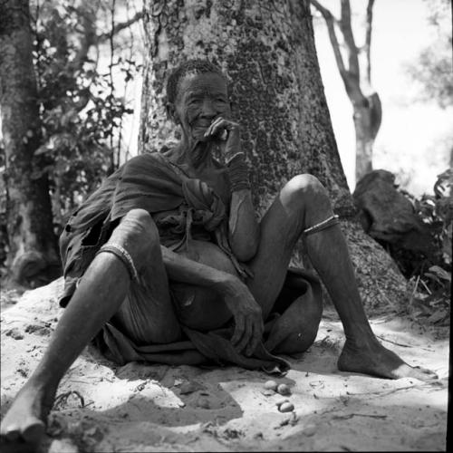 Woman sitting on her kaross, leaning against a tree trunk